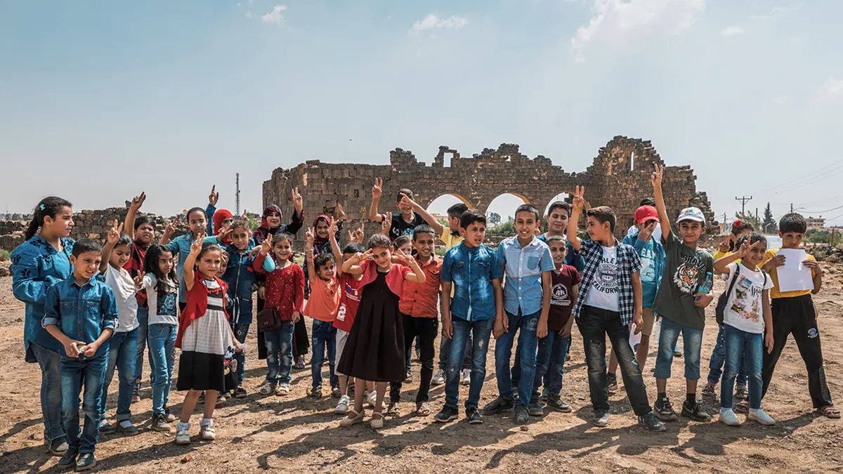 Photograph of local children at Umm Al-Jimal, posing in front of the site's iconic West Church ruins